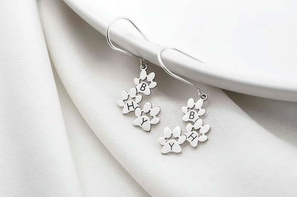 Silver earrings with paw print design on a white fabric background