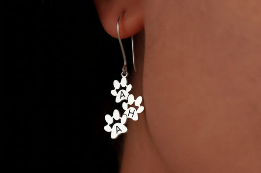 Silver earrings with letter 'A' charms worn on an ear against a dark background