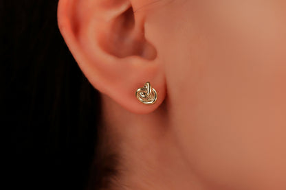 A pair of small dainty stud earrings with a love knot design, held between fingers, showcasing the jewelry's delicate and minimalist design.