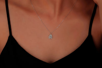 Silver necklace with a leaf pendant on a person wearing a black top.
