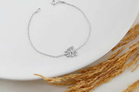 Silver bracelet with leaf charm on a white plate with dried wheat