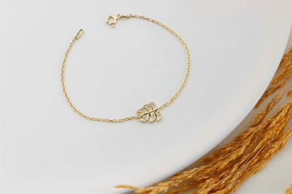 Gold bracelet with leaf charm on a light background