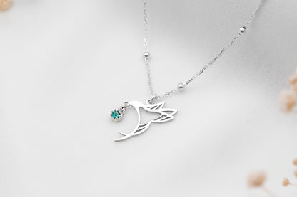 A close-up image of silver-colored necklace with a bird charm and beaded ball chain.