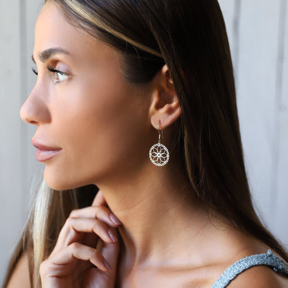 A woman wearing dangle gold mandala earrings with a geometric design, her earrings are gold and the rest of the earrings are silver.