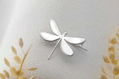 A dainty dragonfly brooch in silver color, attached to a piece of clothing.