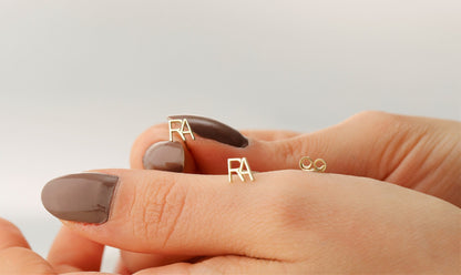 A person's hand displaying a small stud earring with the letter 'A' on the index finger.