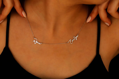A close-up image of a custom two-name necklace made of 14K gold filled, featuring the names in a cursive script.