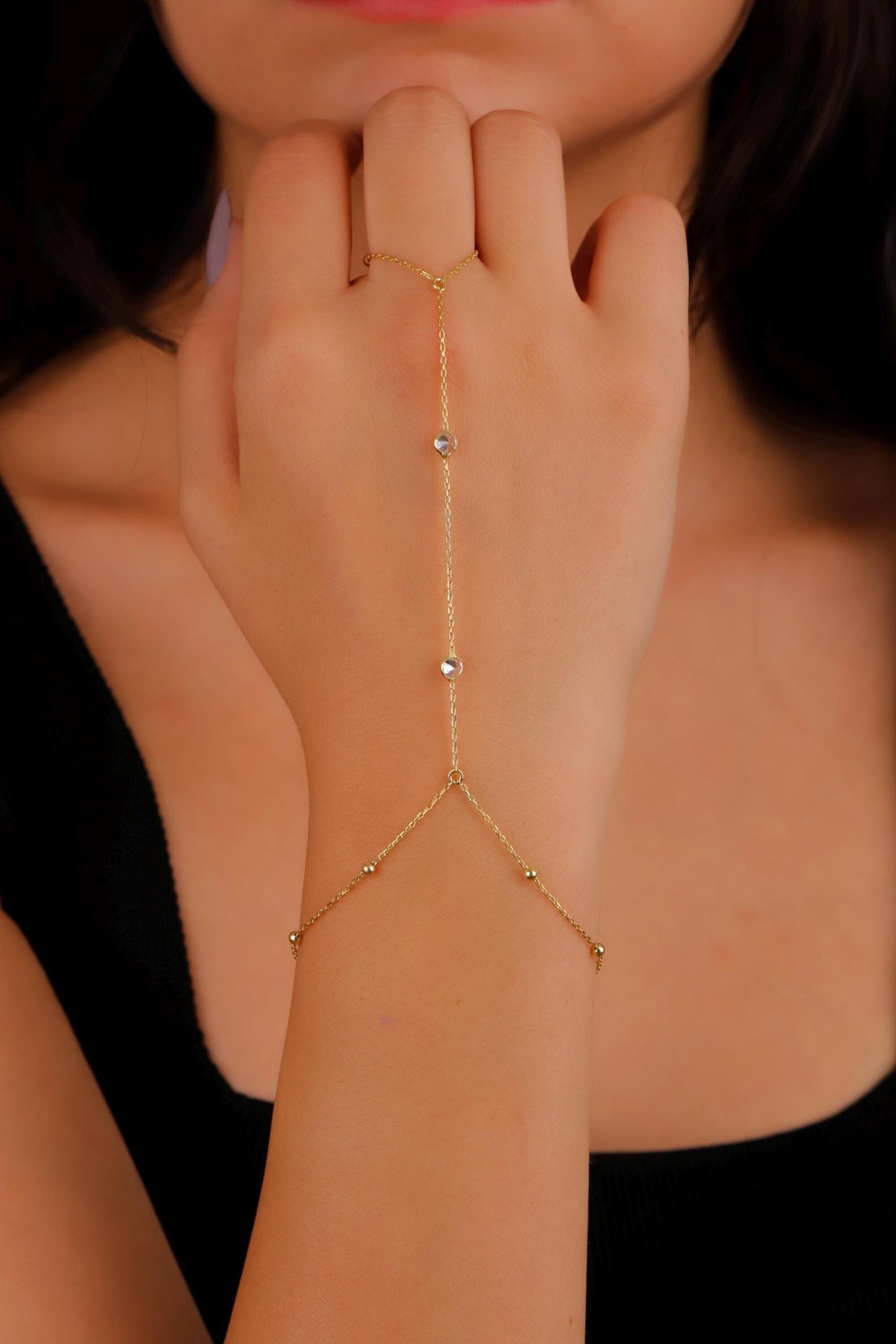 Gold hand chain worn on a hand with a blurred background