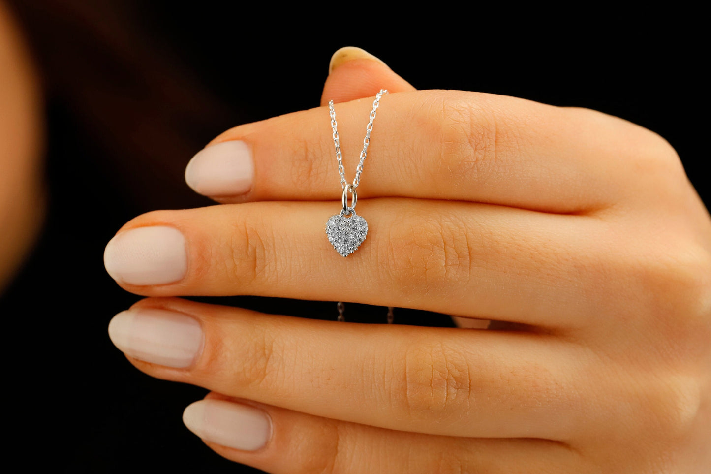 Heart-shaped diamond necklace on a hand against a black background