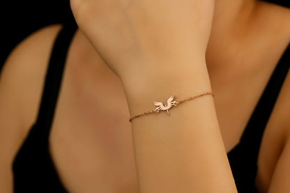 A bracelet with a 14K gold charm in the shape of a phoenix bird, displayed on a person's wrist.
