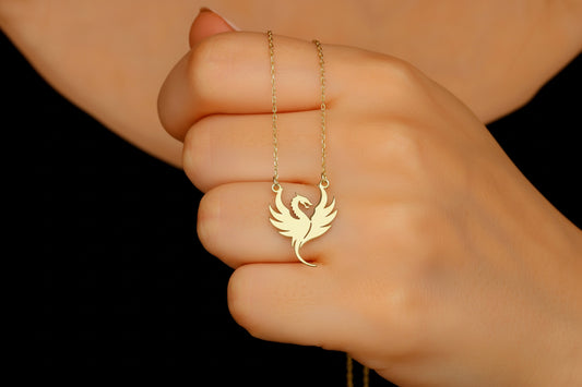 Gold necklace with a bird pendant held by a hand against a black background