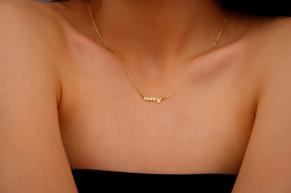 Gold necklace with 'honey' pendant on a person wearing a black top.