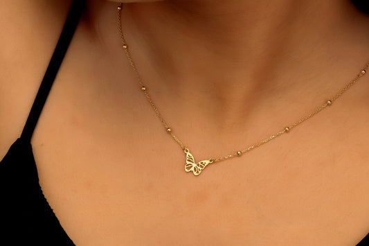 Gold necklace with a butterfly pendant on a person wearing a black top.