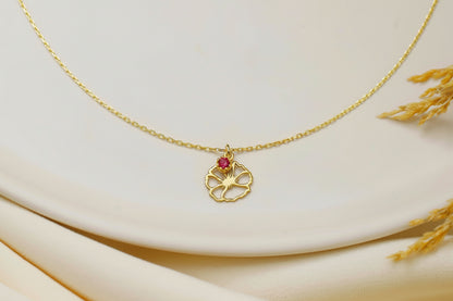 Gold necklace with a pendant featuring a red gemstone on a beige fabric background