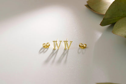 A close-up image of 3 stud earrings with the Roman numerals