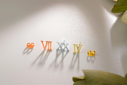 A close-up image of 3 stud earrings with the Roman numerals