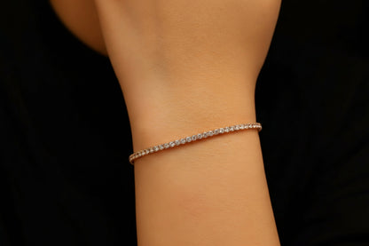 Close-up of a person's wrist wearing a delicate tennis bracelet against a black background
