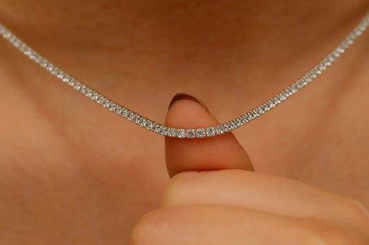 Close-up of a diamond necklace being worn, with a hand holding it against skin.