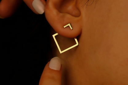A close-up image of a woman's ear wearing a gold-colored square ear jacket earring.