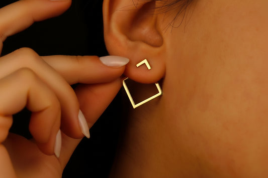 Gold square ear jacket earring being worn on an ear with a hand adjusting it.