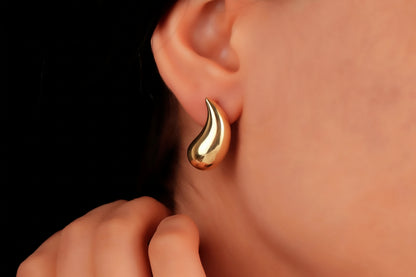 A close-up image of a woman's ear wearing a gold-colored teardrop earring.