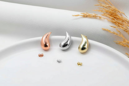 Three teardrop-shaped earrings in rose gold, silver, and gold on a white plate with a light background.