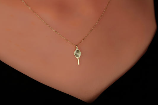 Gold necklace with a tennis racket pendant on a person's neck against a dark background