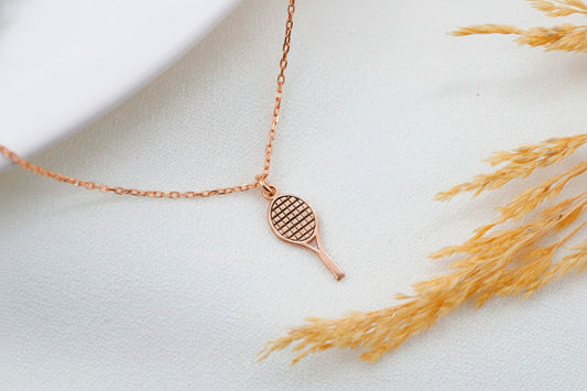 Rose gold necklace with tennis racket pendant on a light background
