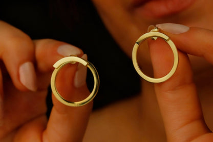 Gold hoop earrings held by a person against a dark background
