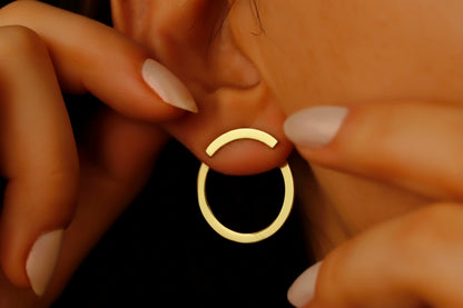 A close-up image of a woman's ear wearing a gold-colored circle ear jacket earring.