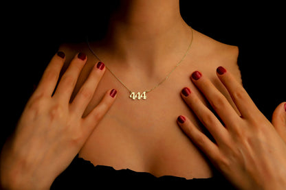 A close-up image of a necklace with the number '444' on a charm, held by a person with red nail polish.
