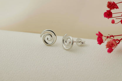 Silver spiral earrings on a white surface with red flowers in the background
