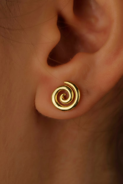 Gold spiral earring on an ear with a blurred background