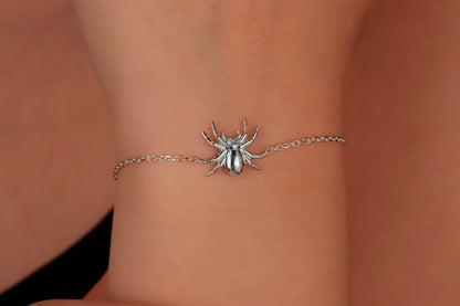 Silver spider bracelet on a wrist against a neutral background