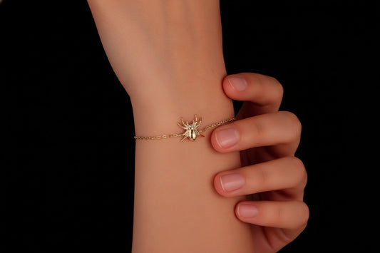 Gold spider bracelet on a wrist against a black background