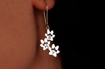 Silver earrings with floral designs and 'BFF' letters worn on an ear against a dark background