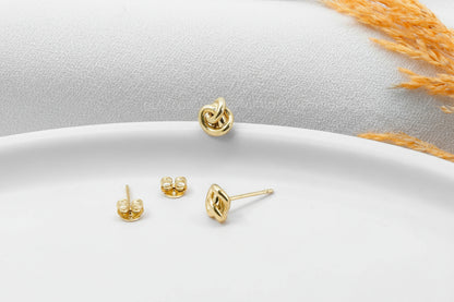 A pair of small dainty stud earrings with a love knot design, held between fingers, showcasing the jewelry's delicate and minimalist design.