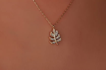 Gold necklace with a leaf-shaped pendant on a brown background