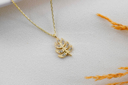 A gold-colored leaf-shaped pendant necklace on a model's neck, showcasing the delicate chain and leaf design.