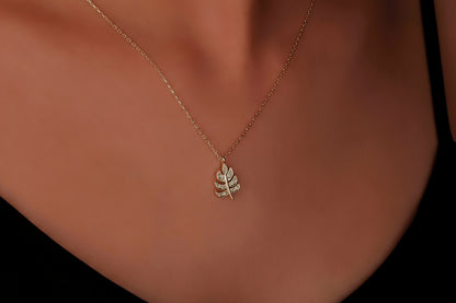 A gold-colored leaf-shaped pendant necklace on a model's neck, showcasing the delicate chain and leaf design.