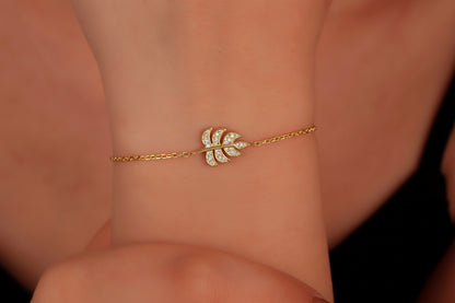 Gold bracelet with leaf design on a wrist against a neutral background