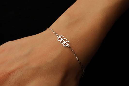 Silver bracelet with the number '666' on a wrist against a black background