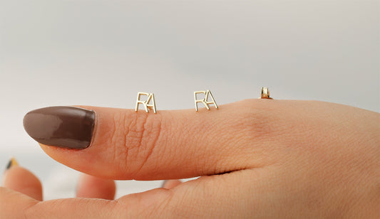 A person's hand displaying a small stud earring with the letter 'A' on the index finger.