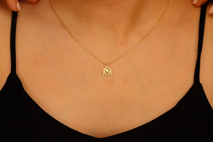 A close-up image of a person wearing a dainty gold monogram necklace with a pendant.