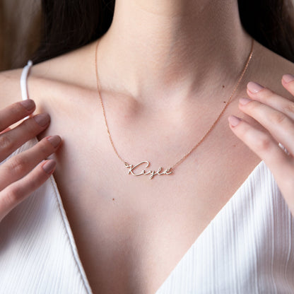 A person wearing a gold personalized name necklace with the name 'Katie' written in a cursive script.