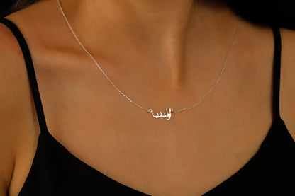 A woman wearing a black tank top showcasing a silver necklace with Arabic script.