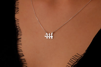 A close-up image of a person wearing a gold necklace with the number 444 on it.