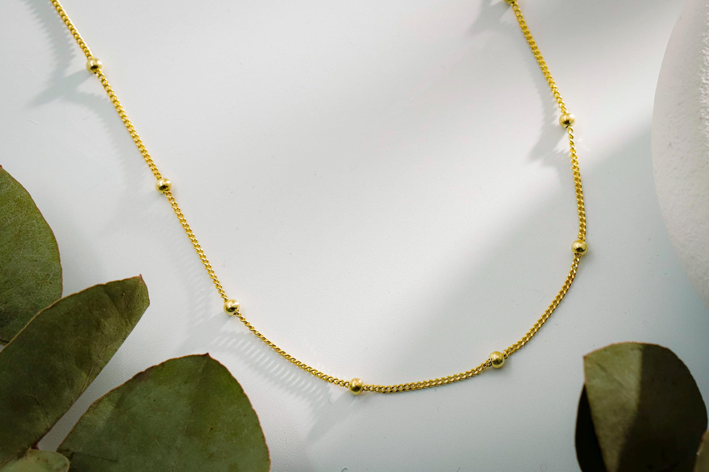Gold necklace on a white surface with green leaves