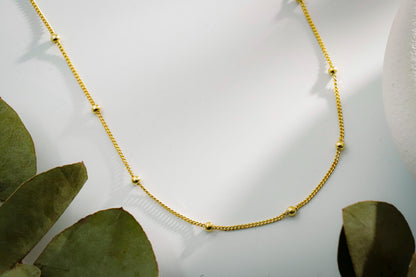 Gold necklace on a white surface with green leaves