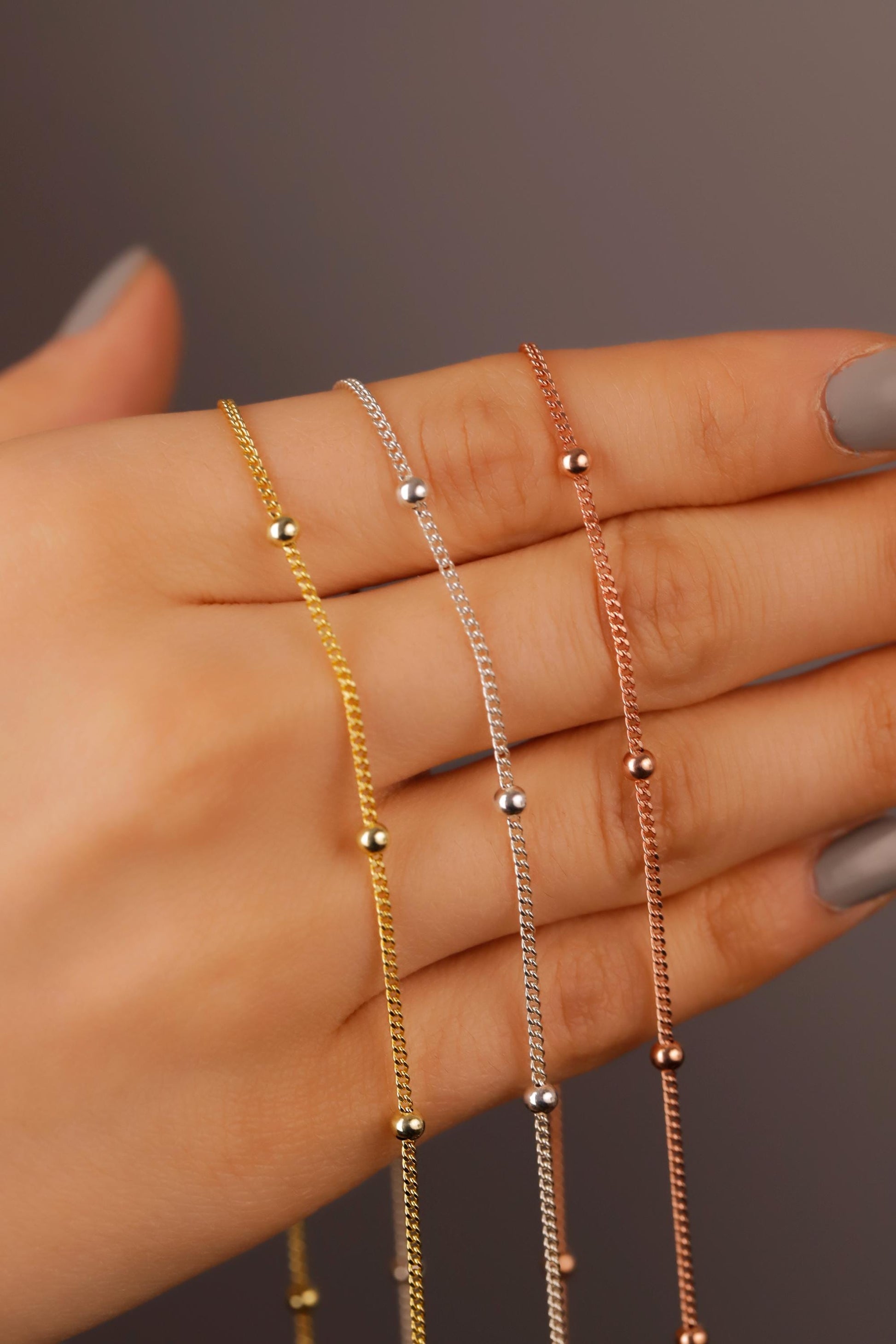 Three gold and silver necklaces on a hand against a neutral background